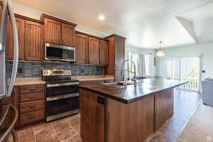 Kitchen with decorative light fixtures, sink, backsplash, stainless steel appliances, and a center island with sink