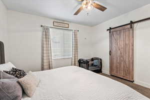 Bedroom featuring ceiling fan, a barn door, and dark colored carpet