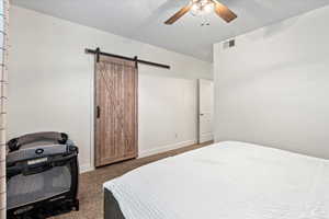 Bedroom featuring ceiling fan, a barn door, and dark colored carpet