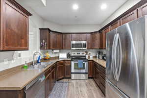 Kitchen with dark brown cabinetry, sink, light hardwood / wood-style floors, and appliances with stainless steel finishes