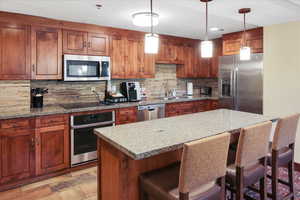 Kitchen featuring pendant lighting, stainless steel appliances, sink, and light stone counters