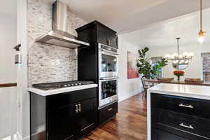 Kitchen with backsplash, dark hardwood / wood-style flooring, hanging light fixtures, stainless steel appliances, and wall chimney range hood