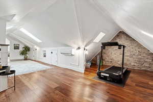 Exercise room with a wall mounted air conditioner, vaulted ceiling with skylight, and hardwood / wood-style floors