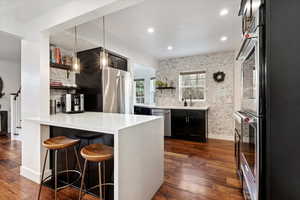 Kitchen featuring dark wood-type flooring, a breakfast bar, hanging light fixtures, appliances with stainless steel finishes, and kitchen peninsula