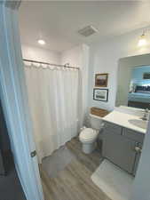 Bathroom with a shower with shower curtain, vanity, toilet, and hardwood / wood-style floors