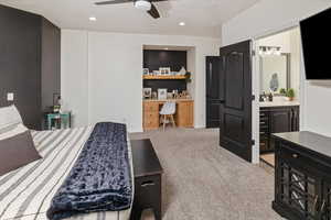 Bedroom featuring ceiling fan, ensuite bathroom, built in desk, and light carpet