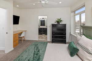 Carpeted bedroom featuring ensuite bathroom, built in desk, and ceiling fan