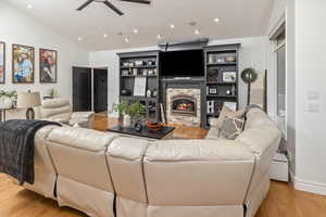 Living room featuring ceiling fan, a stone fireplace, lofted ceiling, and light wood-type flooring