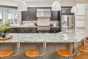 Kitchen with a breakfast bar, sink, high end refrigerator, backsplash, and wall chimney range hood