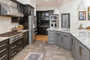 Kitchen with pendant lighting, sink, stainless steel appliances, decorative backsplash, and wall chimney exhaust hood