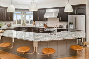 Kitchen with wall chimney range hood, high end refrigerator, and a kitchen breakfast bar