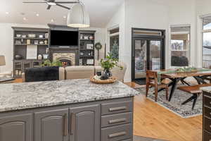 Kitchen featuring gray cabinets, a fireplace, wood-type flooring, hanging light fixtures, and light stone counters