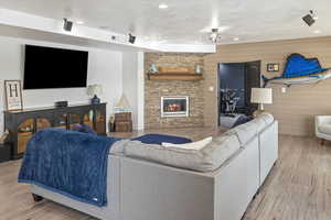 Living room featuring light hardwood / wood-style flooring, a stone fireplace, wooden walls, and a textured ceiling