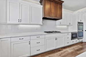 Kitchen featuring stainless steel appliances, light hardwood / wood-style floors, decorative backsplash, and white cabinets