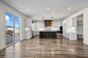 Kitchen with light hardwood / wood-style flooring, appliances with stainless steel finishes, white cabinetry, a kitchen island, and decorative light fixtures