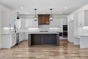 Kitchen featuring hanging light fixtures, a kitchen island, white cabinets, and appliances with stainless steel finishes