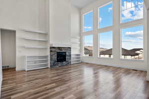 Unfurnished living room featuring hardwood / wood-style flooring, a stone fireplace, a high ceiling, and built in shelves