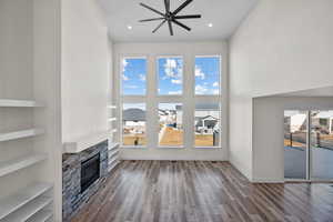 Unfurnished living room with a stone fireplace, hardwood / wood-style floors, built in features, and ceiling fan