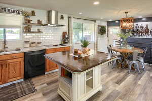 Kitchen featuring wall chimney exhaust hood, sink, tasteful backsplash, decorative light fixtures, and black appliances