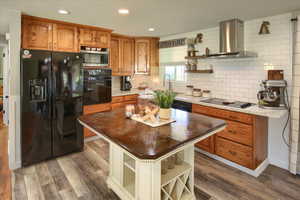 Kitchen featuring tasteful backsplash, sink, hardwood / wood-style flooring, black appliances, and wall chimney exhaust hood