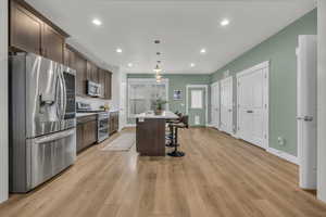 Kitchen featuring a kitchen bar, dark brown cabinets, appliances with stainless steel finishes, a kitchen island, and pendant lighting