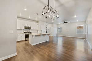 Kitchen featuring white cabinets, a kitchen breakfast bar, hanging light fixtures, a kitchen island with sink, and stainless steel appliances