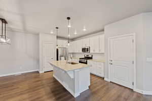 Kitchen with stainless steel appliances, white cabinetry, a kitchen island with sink, and pendant lighting