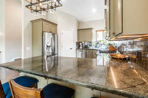 Kitchen featuring tasteful backsplash, appliances with stainless steel finishes, decorative light fixtures, and a breakfast bar