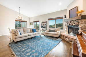 Living room featuring an inviting chandelier, a fireplace, vaulted ceiling, and hardwood flooring