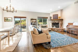 Living room featuring a stone fireplace, hardwood  floors, and a chandelier