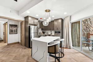 Kitchen featuring appliances with stainless steel finishes, a center island, light stone countertops, dark brown cabinets, and wall chimney exhaust hood