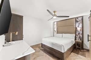 Bedroom with light parquet floors, a barn door, and ceiling fan