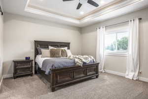 Carpeted bedroom featuring ceiling fan and a raised ceiling