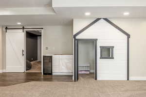 Interior space with wine cooler, a barn door, and dark colored carpet