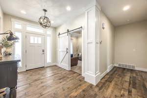 Foyer with dark wood-type flooring, a barn door, and a chandelier