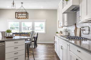 Kitchen featuring dark wood-type flooring, white cabinetry, hanging light fixtures, backsplash, and stainless steel gas cooktop