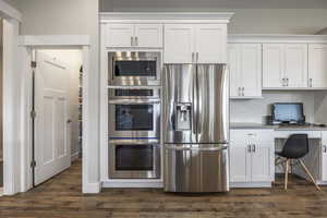 Kitchen with white cabinetry, stainless steel appliances, dark hardwood / wood-style floors, and built in desk