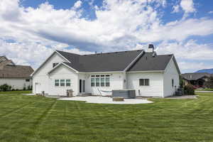 Back of property with a lawn, a hot tub, a patio, and central air condition unit