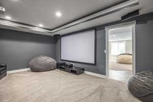 Carpeted home theater room featuring ornamental molding and a raised ceiling