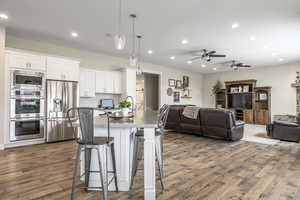 Kitchen featuring hanging light fixtures, white cabinetry, appliances with stainless steel finishes, and a breakfast bar