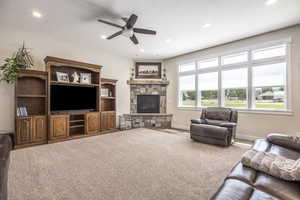 Carpeted living room featuring ceiling fan, a stone fireplace, and a textured ceiling