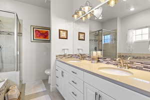 Bathroom with a shower with shower door, backsplash, vanity, toilet, and tile patterned floors