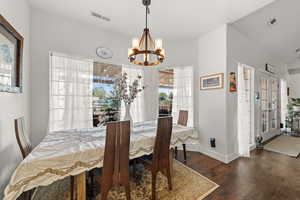 Dining area featuring a notable chandelier, dark wood-type flooring, french doors, and vaulted ceiling