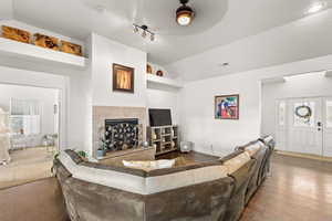 Living room featuring a tiled fireplace, vaulted ceiling, dark wood-type flooring, and track lighting