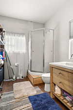 Bathroom with a shower with door, vanity, wood-type flooring, and toilet