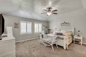 Carpeted bedroom featuring ceiling fan, a textured ceiling, a tray ceiling, and lofted ceiling