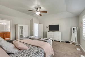 Bedroom with ceiling fan, ensuite bathroom, light colored carpet, and lofted ceiling