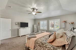 Carpeted bedroom with ceiling fan, a textured ceiling, and a tray ceiling