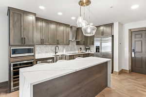 Kitchen featuring appliances with stainless steel finishes, decorative light fixtures, sink, beverage cooler, and wall chimney exhaust hood