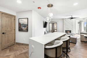 Kitchen with pendant lighting, light parquet floors, a high end fireplace, light stone countertops, and a kitchen bar